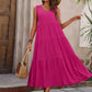 Woman in vibrant pink tiered maxi dress, straw hat, and woven bag for summer fashion