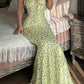Woman in yellow floral maxi dress with tie straps, sitting on bed in cozy bedroom
