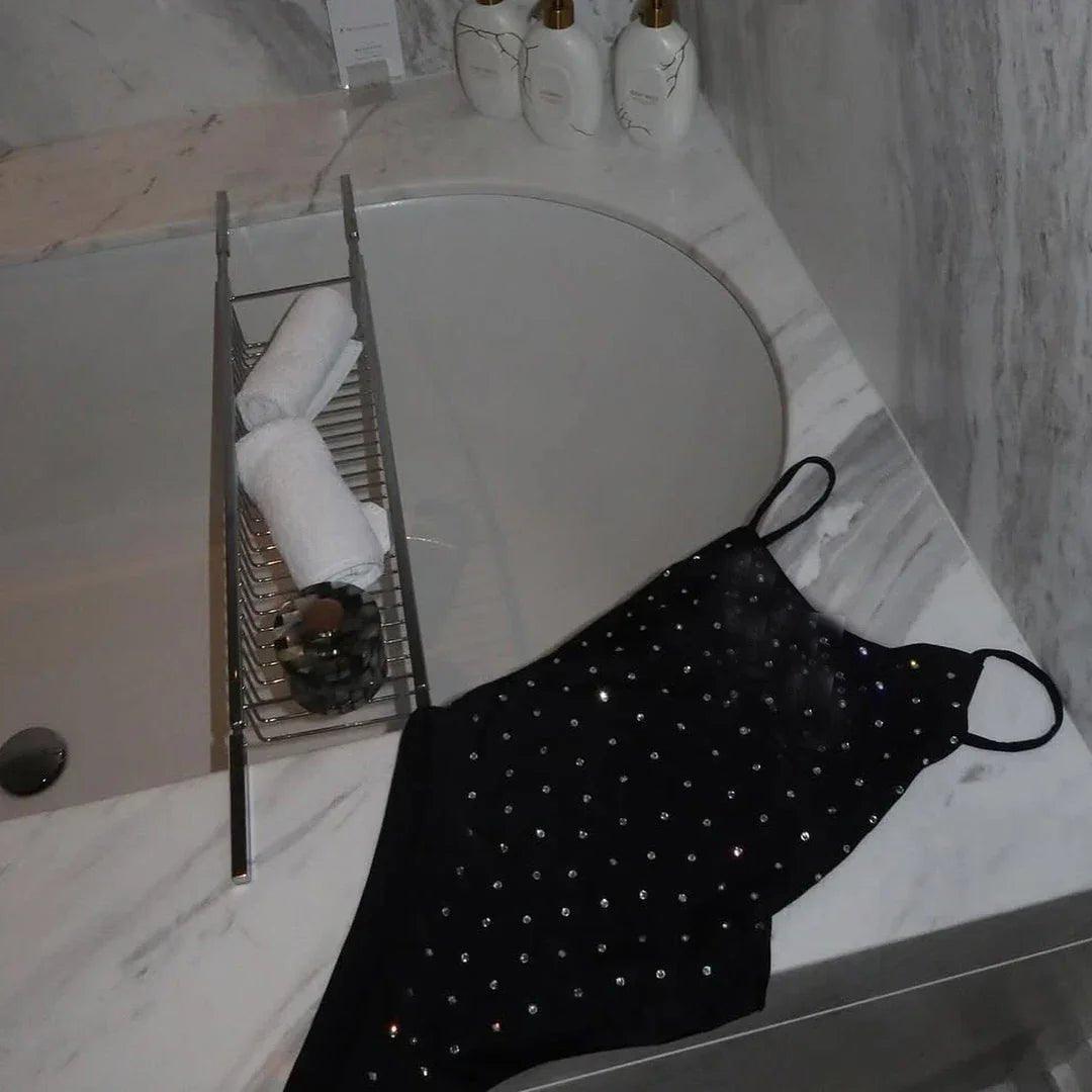 Black rhinestone-embellished camisole on marble bathroom counter beside bathtub with towel rack