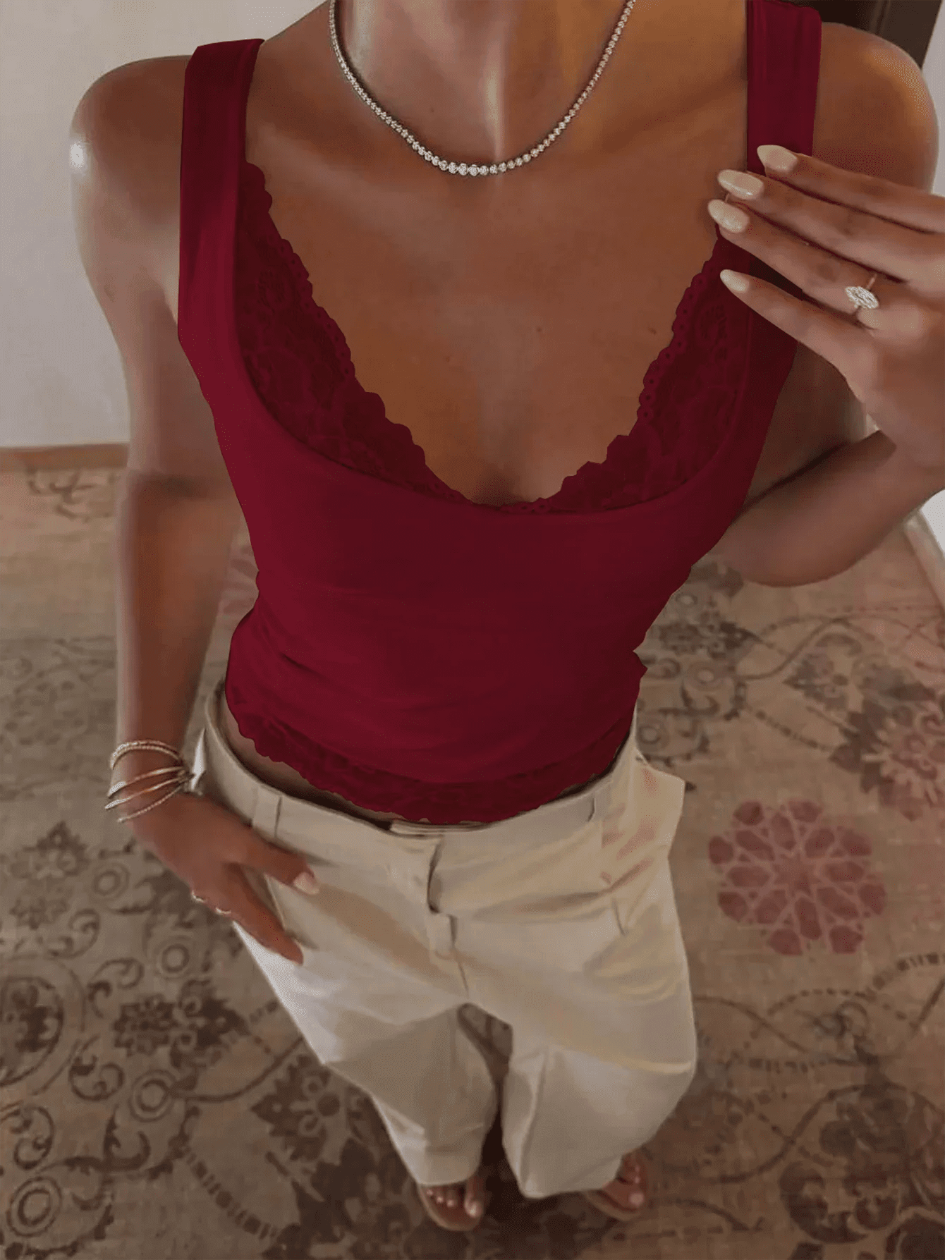 Woman wearing burgundy lace trim tank top with white pants, diamond necklace, and ring for stylish fashion look