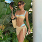 Woman in yellow and blue floral bikini with wrap skirt, holding camera near tropical leaves