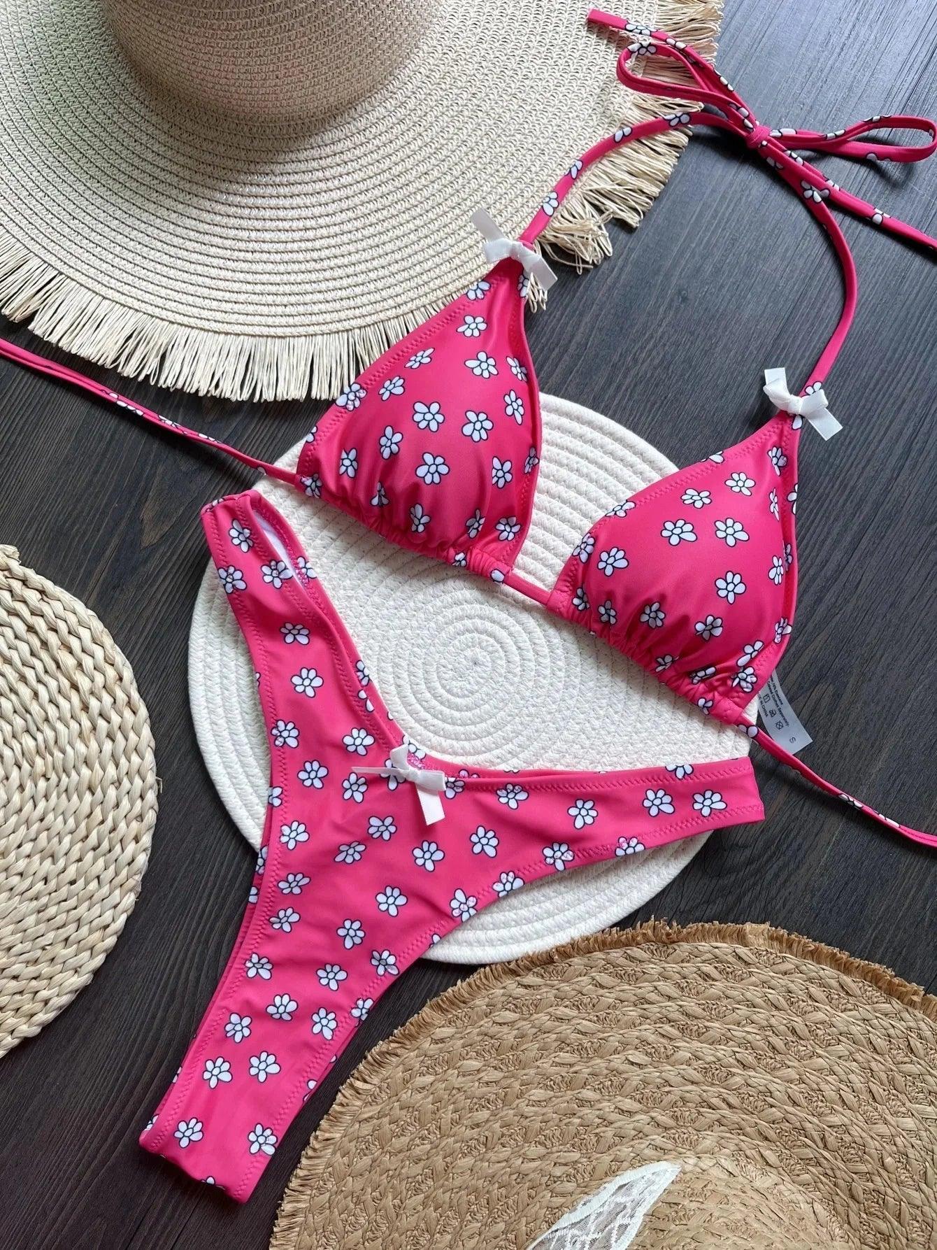Pink floral bikini set with white daisy print, triangle top and thong bottom, styled with straw hats for summer beach fashion.