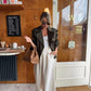 Woman in olive trench coat, white top, wide-leg pants, sunglasses, and tan handbag at café