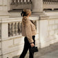 Woman in beige trench coat with black bow hair accessory, carrying quilted handbag, stylish street fashion
