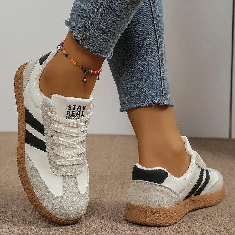 White and black retro sneakers with 'STAY REAL' text, worn with jeans and anklet, women's fashion footwear