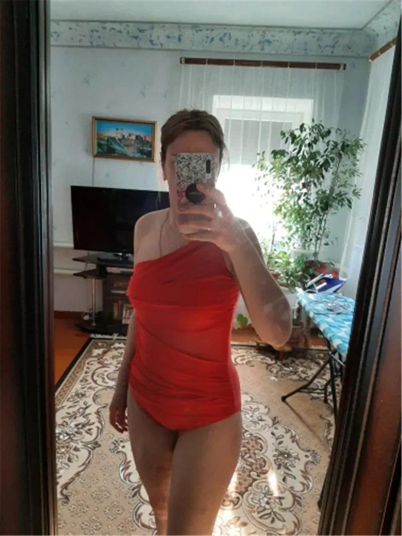 Woman in red one-shoulder swimsuit taking mirror selfie at home, fashion swimwear style