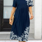 Navy blue women's midi dress with white lace print, short sleeves, and pleated waist, styled with straw clutch