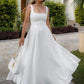Woman in elegant white midi dress with square neckline, twirling outdoors with white handbag and heels