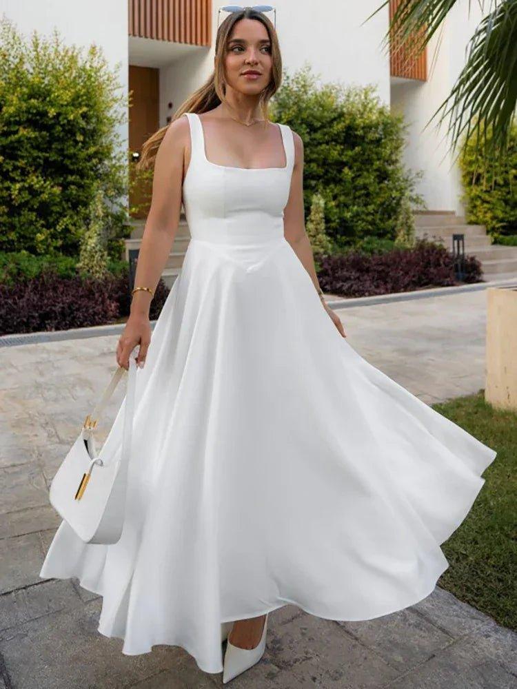 Woman in elegant white midi dress with square neckline, twirling outdoors with white handbag and heels