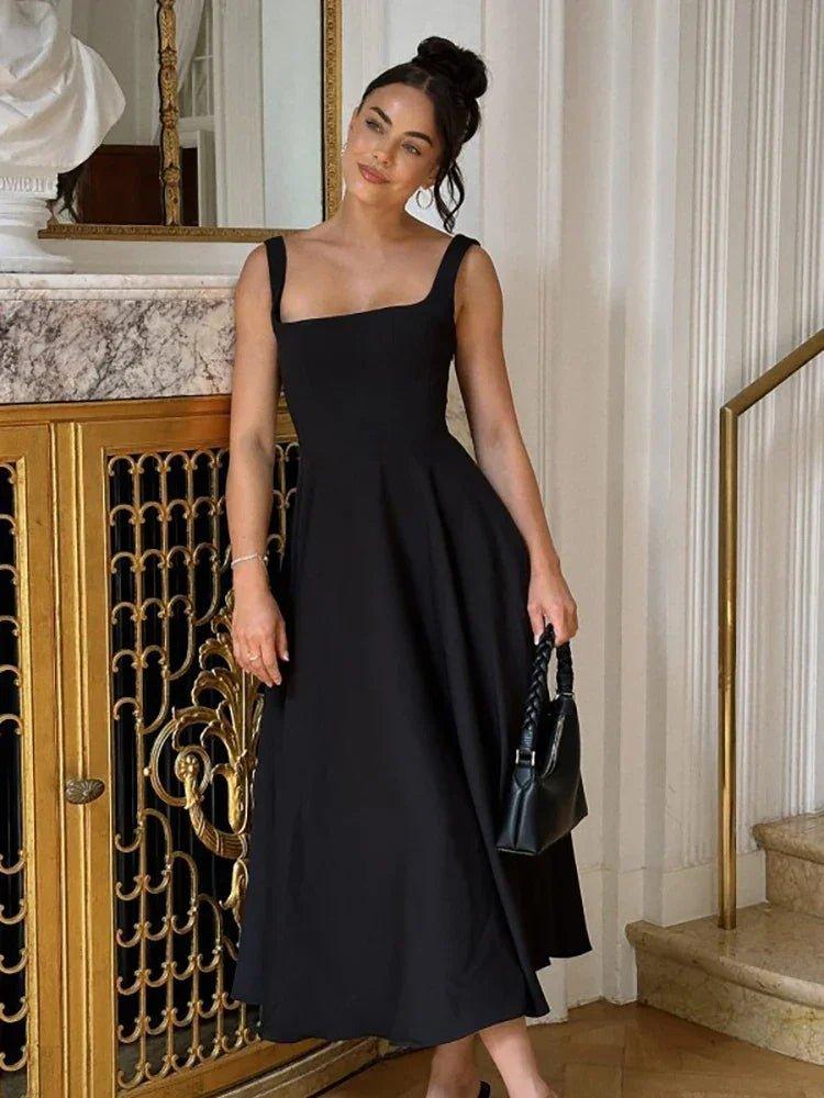 Woman in elegant black midi dress with square neckline, holding braided handbag, luxury fashion