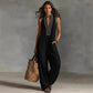 Woman in black sleeveless jumpsuit with white embroidery, carrying straw tote bag, fashion outfit
