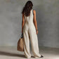 Woman in beige sleeveless wide-leg jumpsuit with straw bag, back view