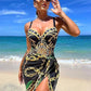 Woman in stylish black and gold chain print beach dress with high slit, sunglasses, ocean backdrop
