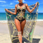 Woman in black gold patterned one-piece swimsuit with matching beach cover-up on sandy shore