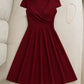 Burgundy V-neck wrap dress with short sleeves and flared skirt, styled with gold necklace on beige sofa