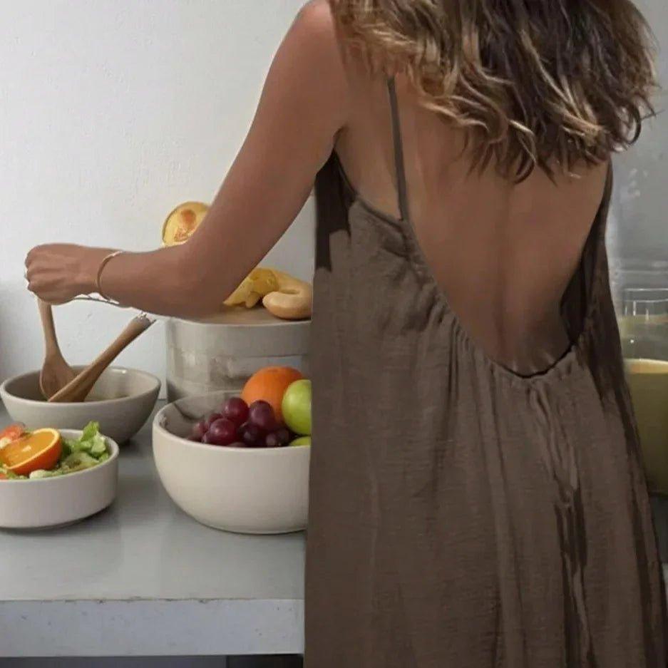 Woman in backless brown dress preparing salad with fresh fruits in kitchen